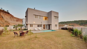 A modern two-story house with a swimming pool, outdoor seating, and a view of a hillside. - ELIVAAS 3 BHK Villa Shourya Bliss (Udaipur)