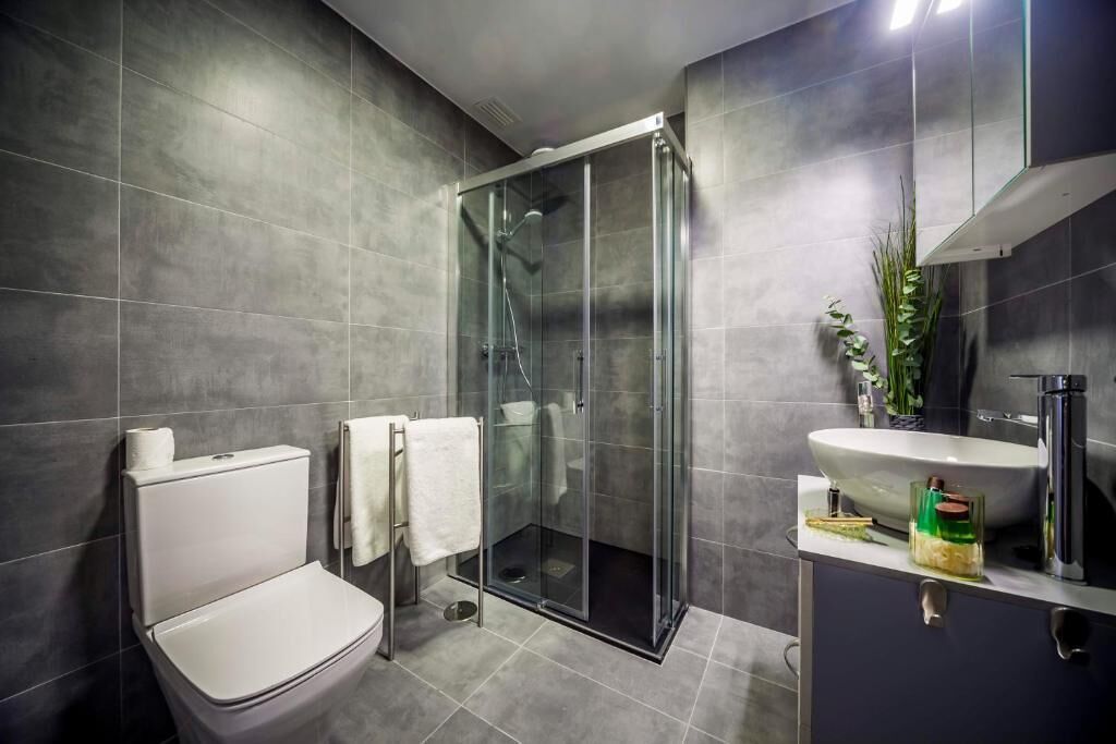 Een moderne badkamer met een douchecabine van glas, een toilet, een wastafel en een spiegel.
