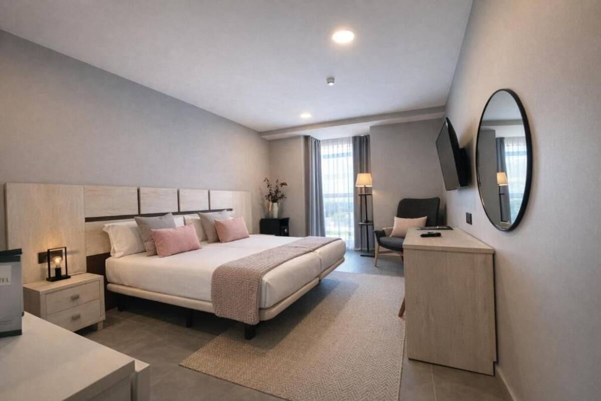 A modern bedroom with a bed, bedside tables, a desk, a chair, a TV, and a mirror.