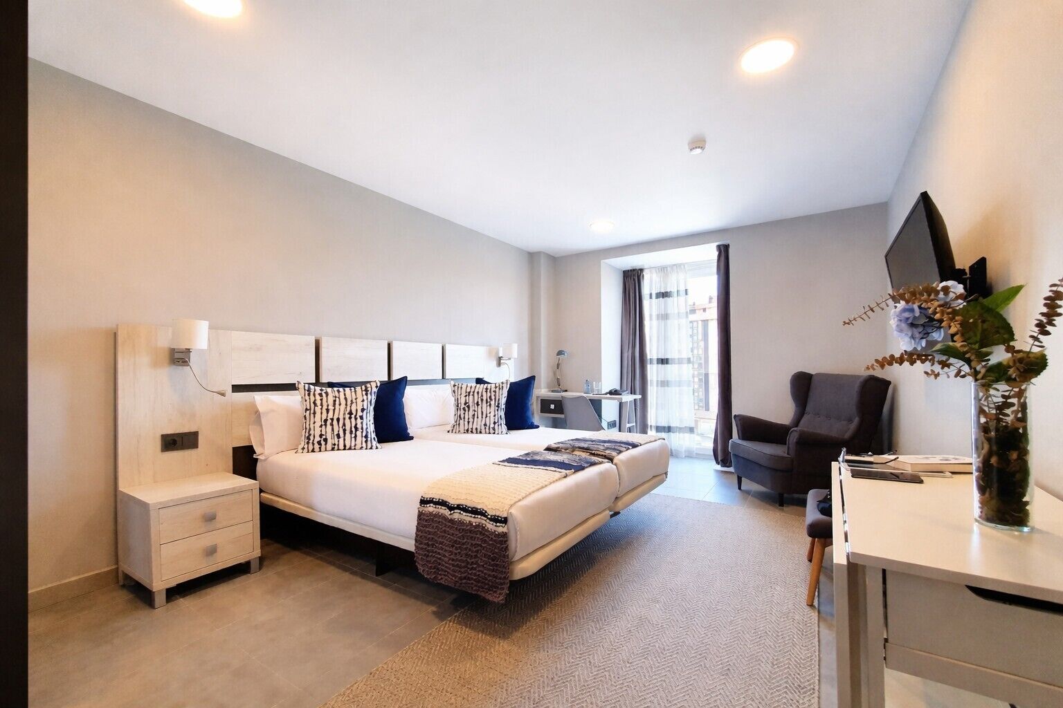 Een moderne hotelkamer met een groot bed, nachtkastjes, een bureau, een stoel en een groot raam.