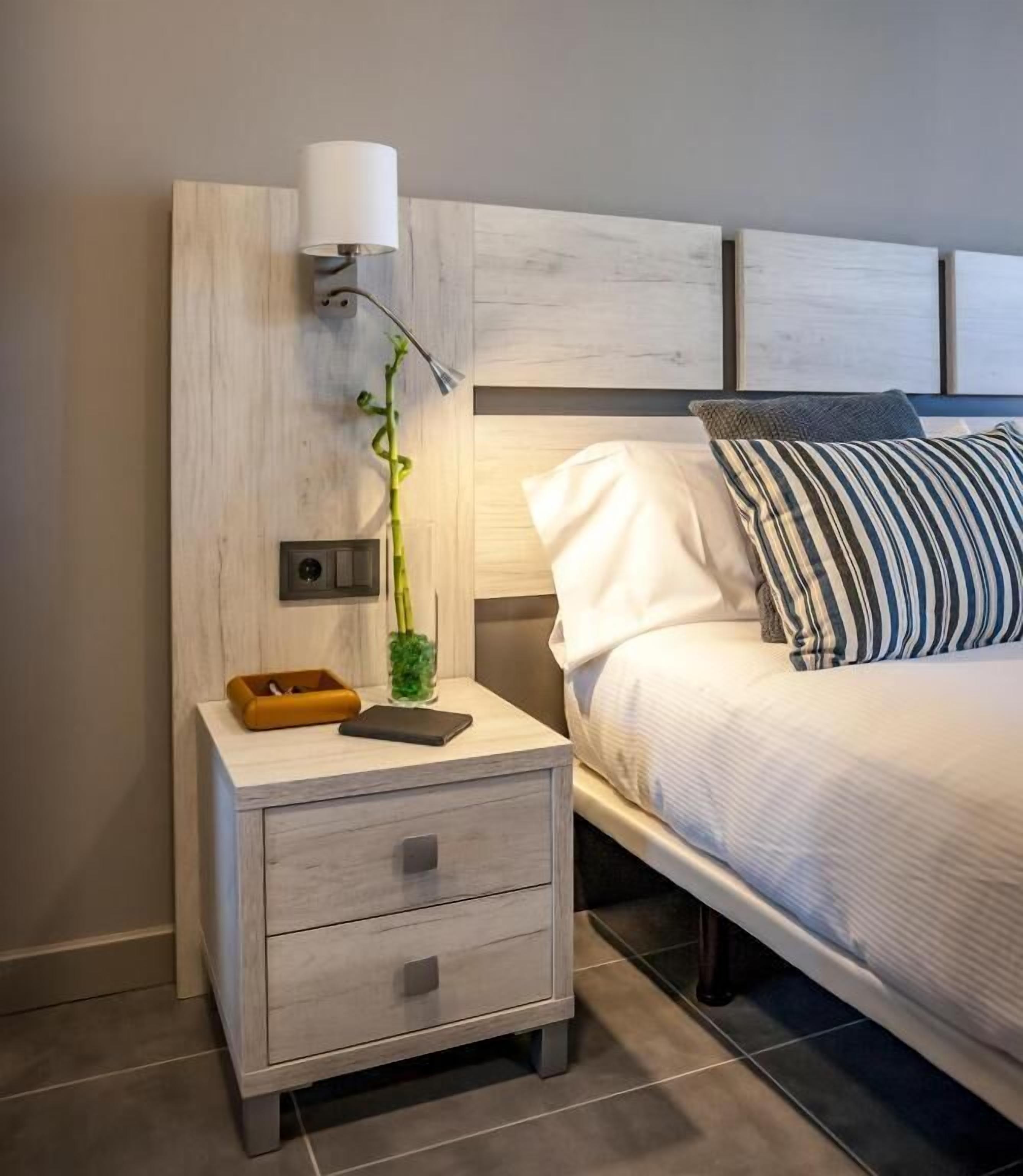 A bedroom with a bed, bedside table, lamp, and a small plant.