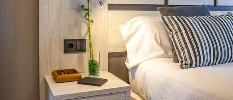 A bedroom with a bed, bedside table, lamp, and a small plant.