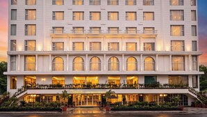 Een hotel met meerdere verdiepingen, een opvallend bord met 'TRINITY HOTEL', diverse balkons en een restaurant genaamd 'Kuzina' op de begane grond.