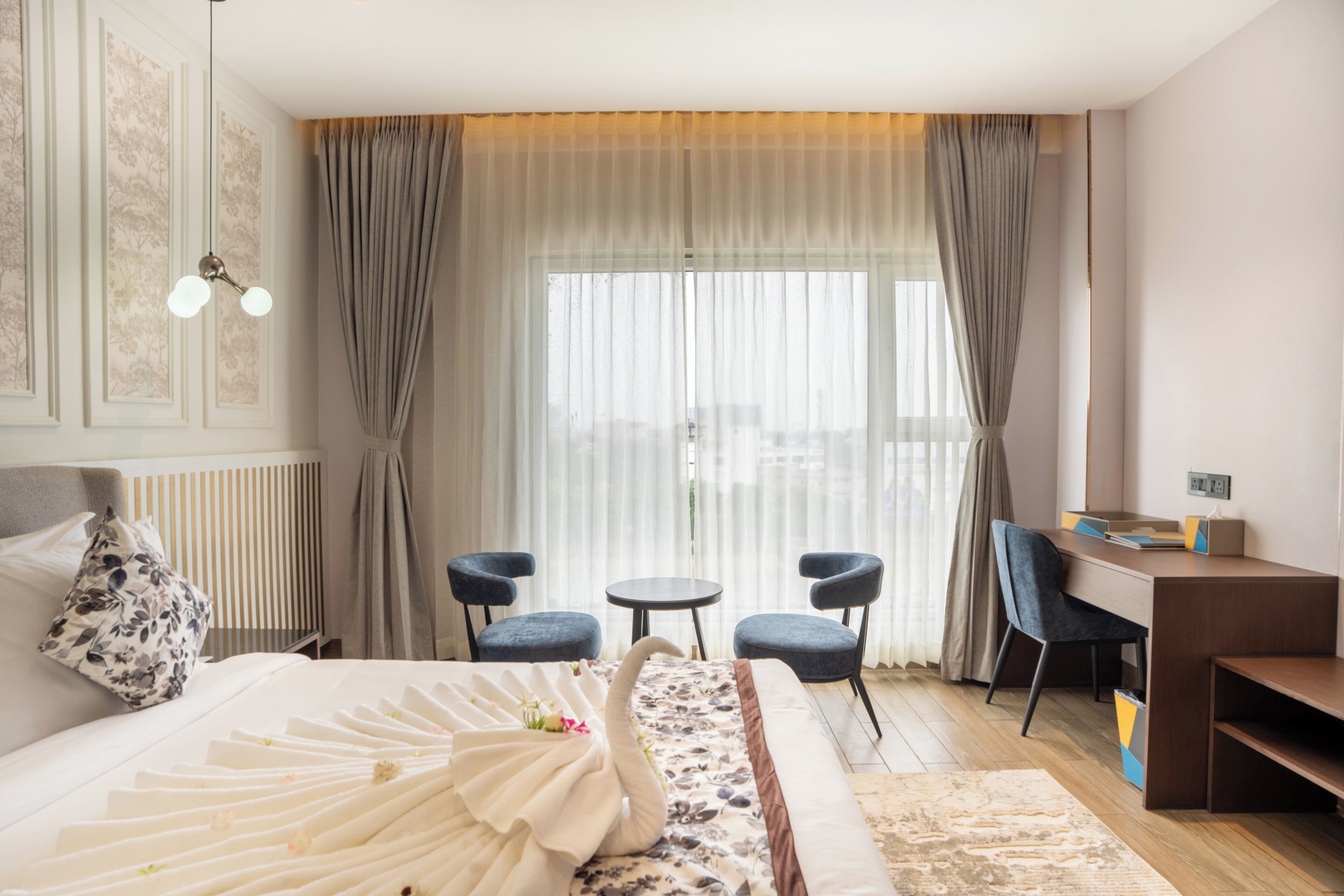 A hotel room with a bed, two chairs, a desk, and a window with curtains.