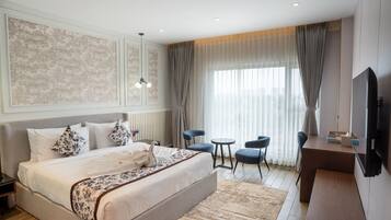 A hotel room with a large bed, a desk, two chairs, a TV, and a window with curtains.