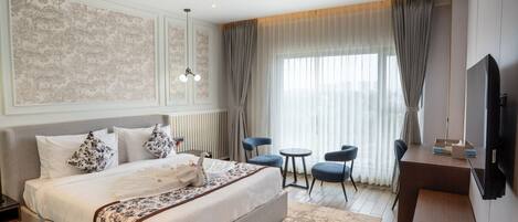 Habitación de hotel con una cama grande, un escritorio, dos sillas, un televisor y una ventana con cortinas.