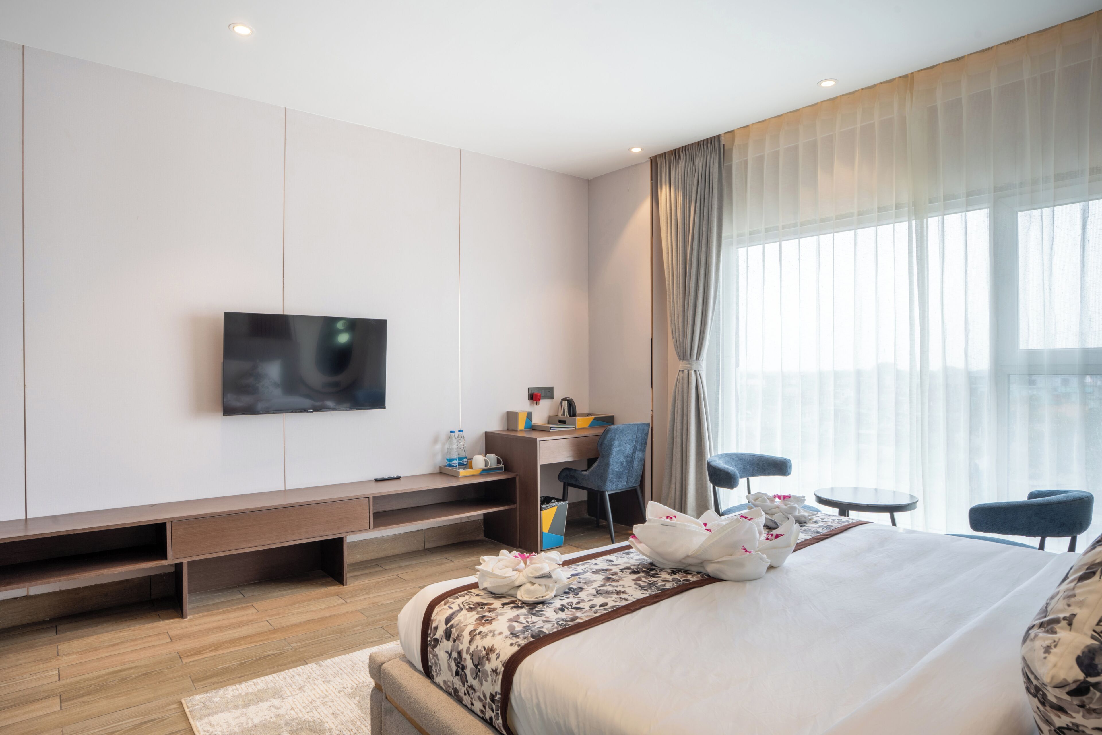 Une chambre d’hôtel moderne dotée d’un grand lit, d’un bureau avec une chaise, d’un téléviseur fixé au mur et d’une grande fenêtre avec des rideaux.
