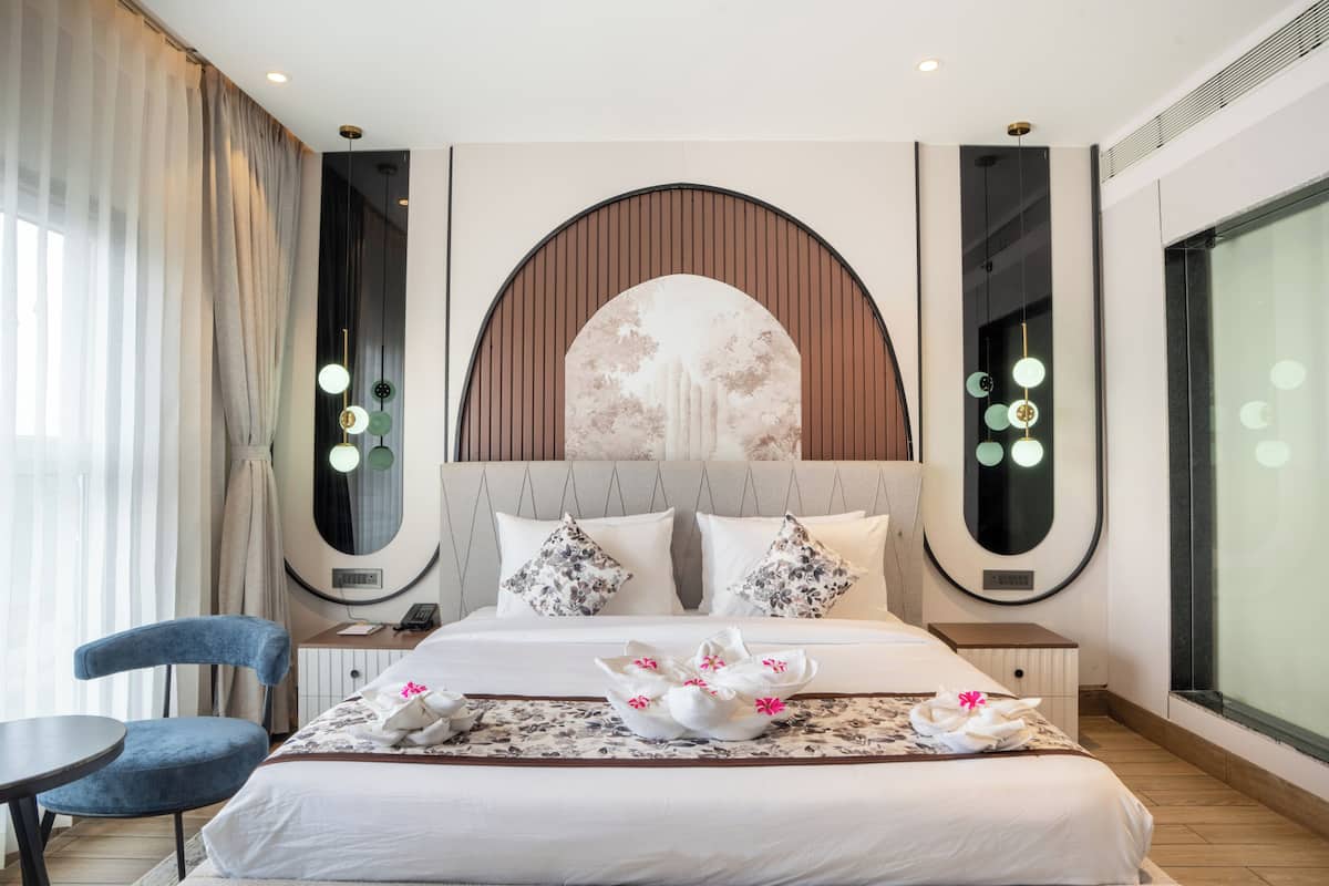 A hotel room with a large bed, a desk, a chair, and a large window.