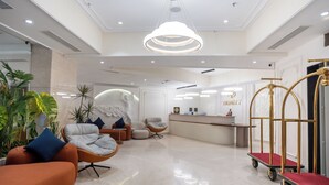 Een moderne hotellobby met een receptiebalie, comfortabele zithoek en een decoratieve kroonluchter.