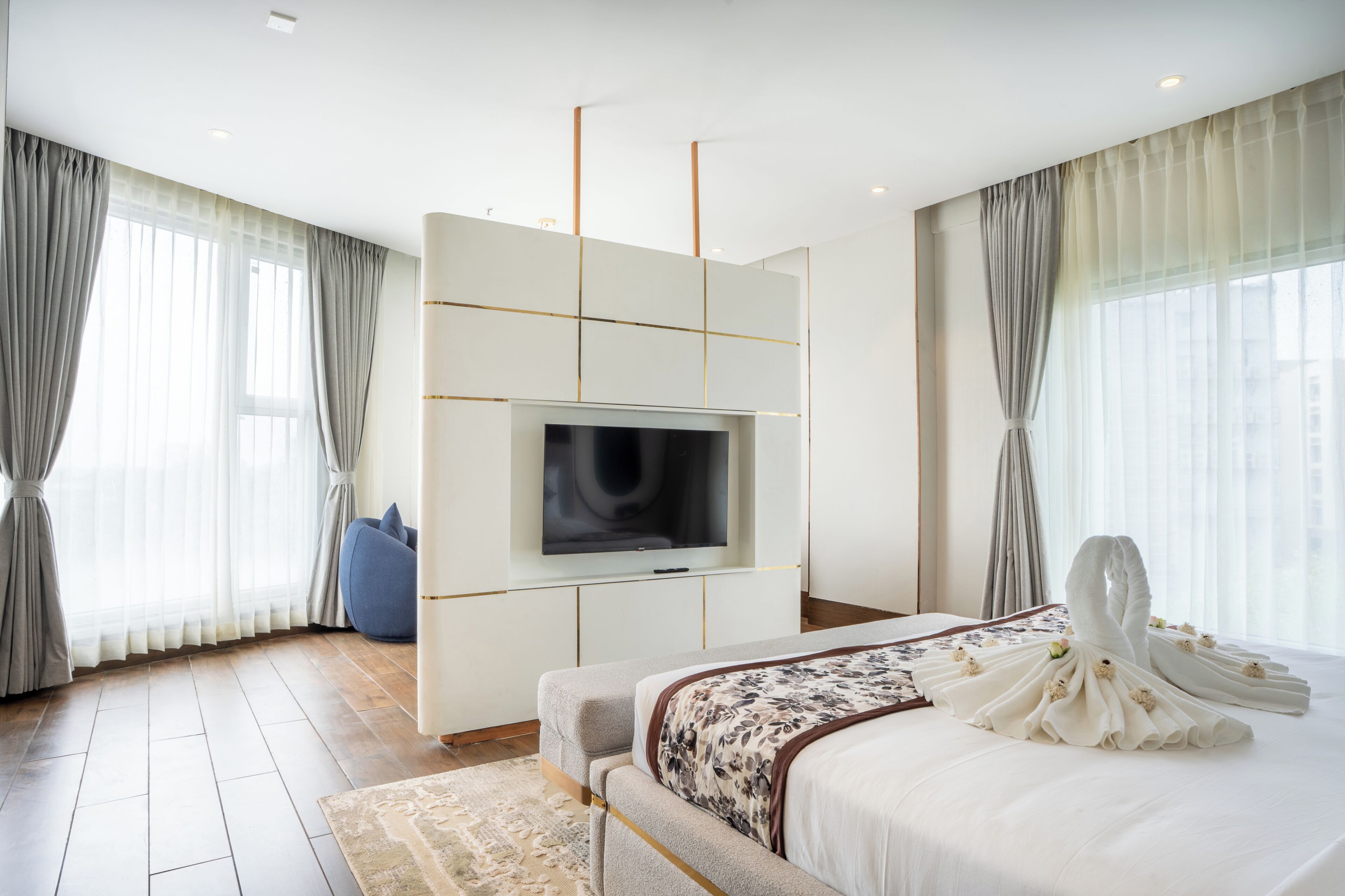 Une chambre d’hôtel moderne dotée d’un grand lit, d’un téléviseur à écran plat fixé au mur, d’un canapé et d’une grande fenêtre avec des rideaux.