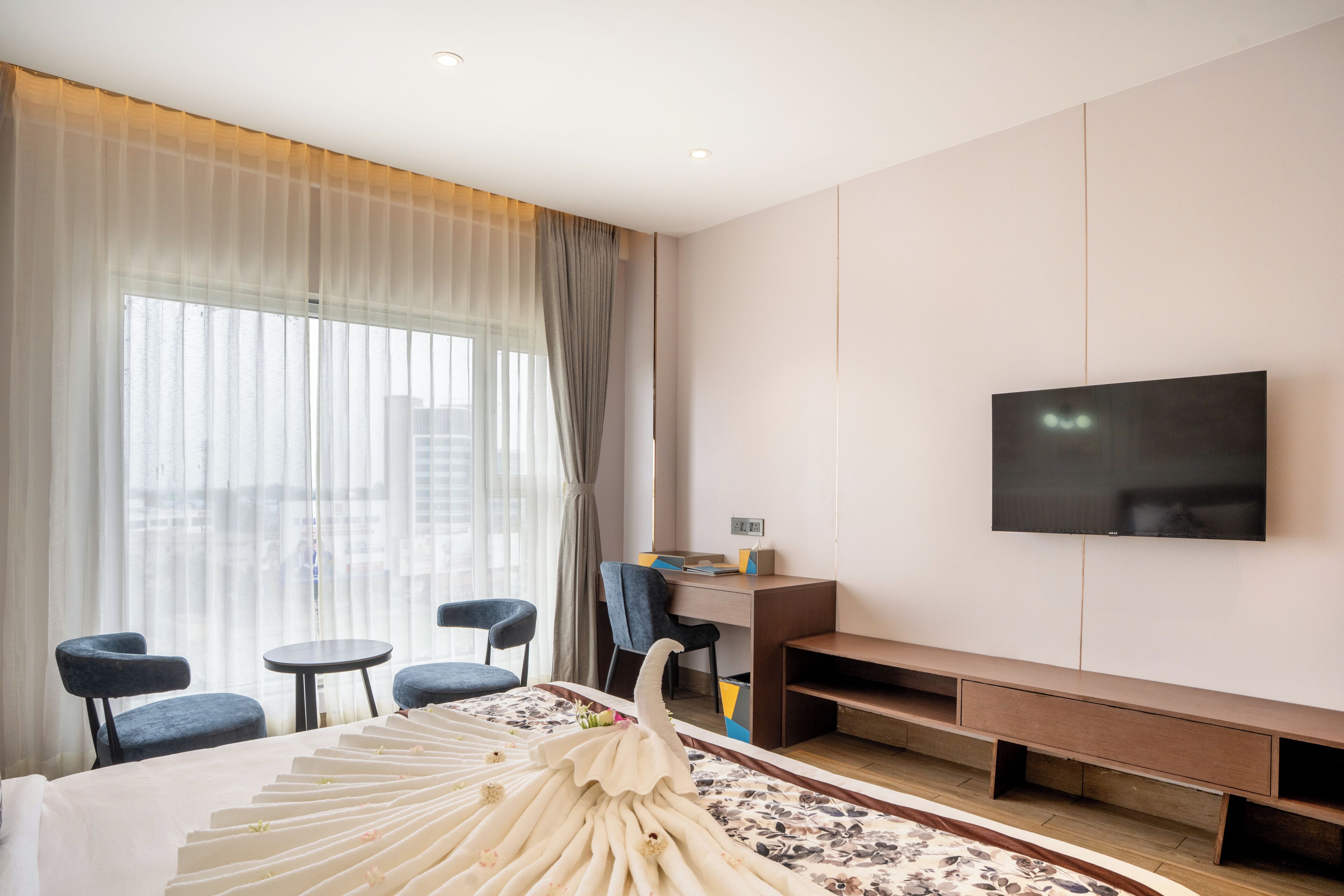 A hotel room with a bed, a TV mounted on the wall, a desk, and two chairs.
