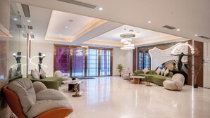 Een ruime lobby met een modern design, met een groene bank, een witte fauteuil en een ronde tafel.