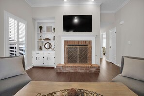 Una sala de estar con chimenea, televisión y armarios blancos.