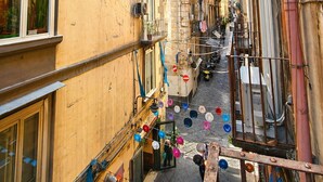 A narrow street with buildings on either side, balconies with plants, and a clear blue sky. - Cuevas Home Relais  (Naples)