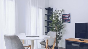 En moderne stue med et rundt bord, to stole, et fjernsyn, en bogreol og en potteplante.