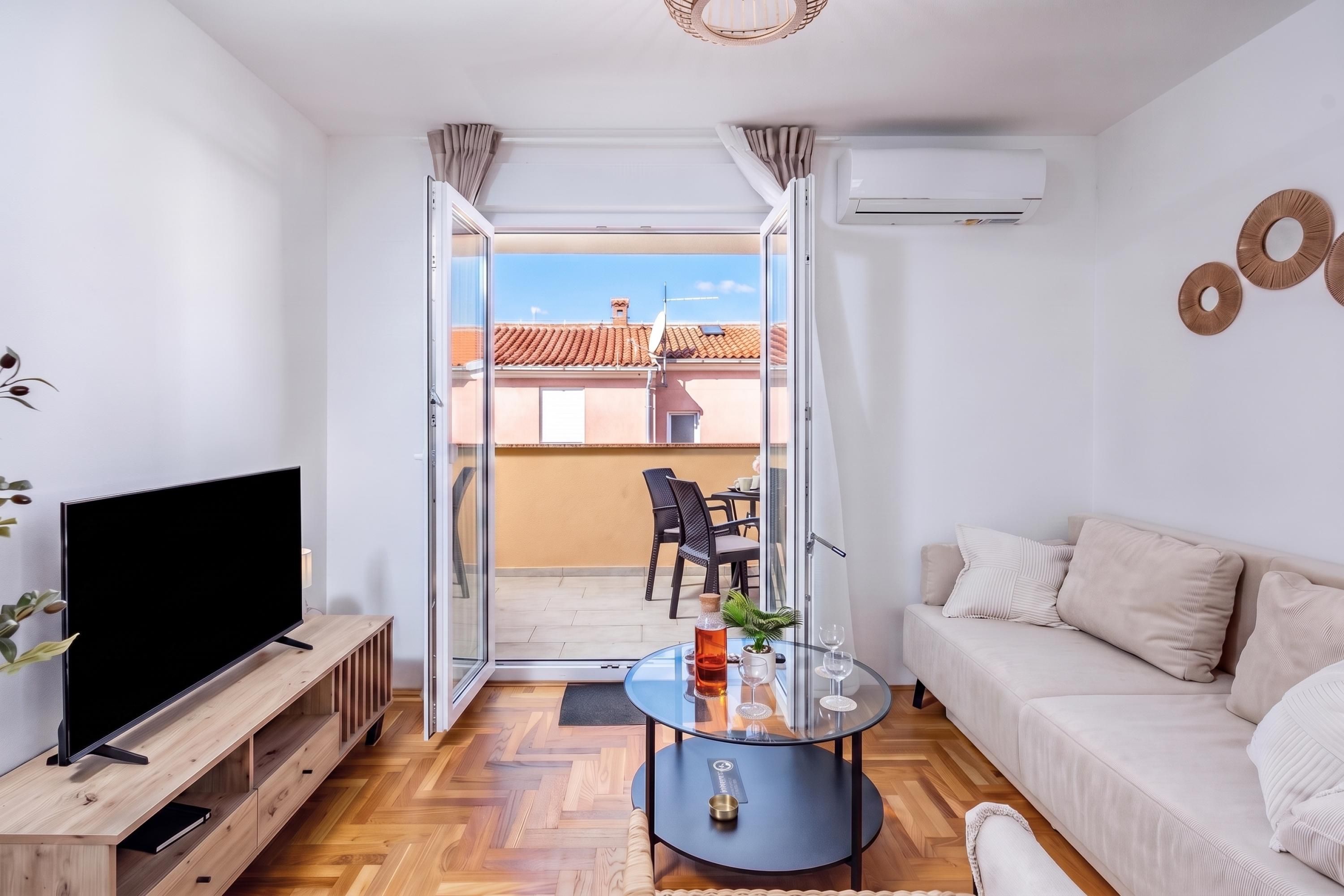 Uma sala moderna com televisão de tela plana, sofá, mesa de centro e varanda com vista para edifícios.
