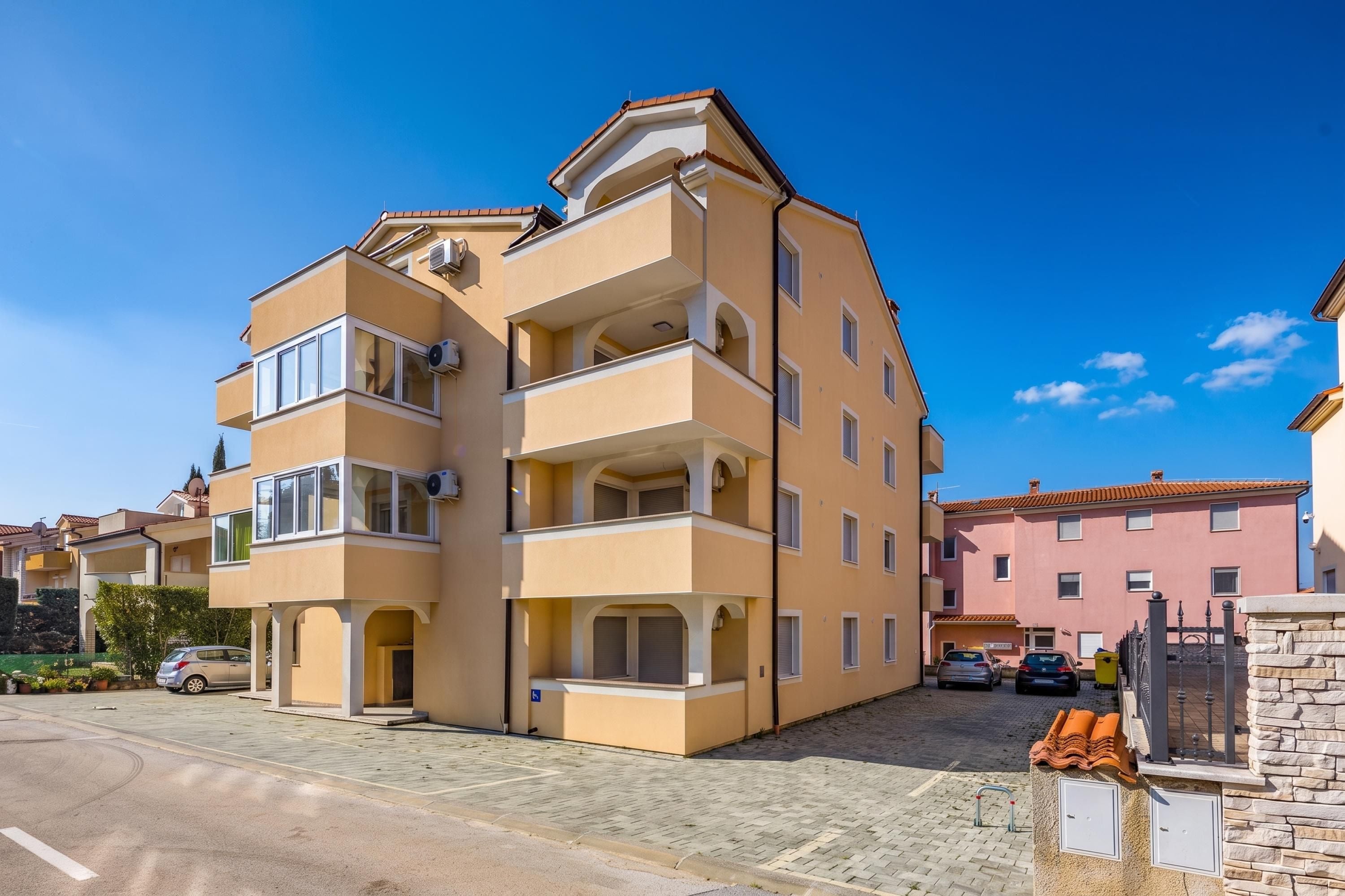 Un edifici residencial de diversos pisos amb terrat pla, balcons i una zona d'entrada pavimentada.