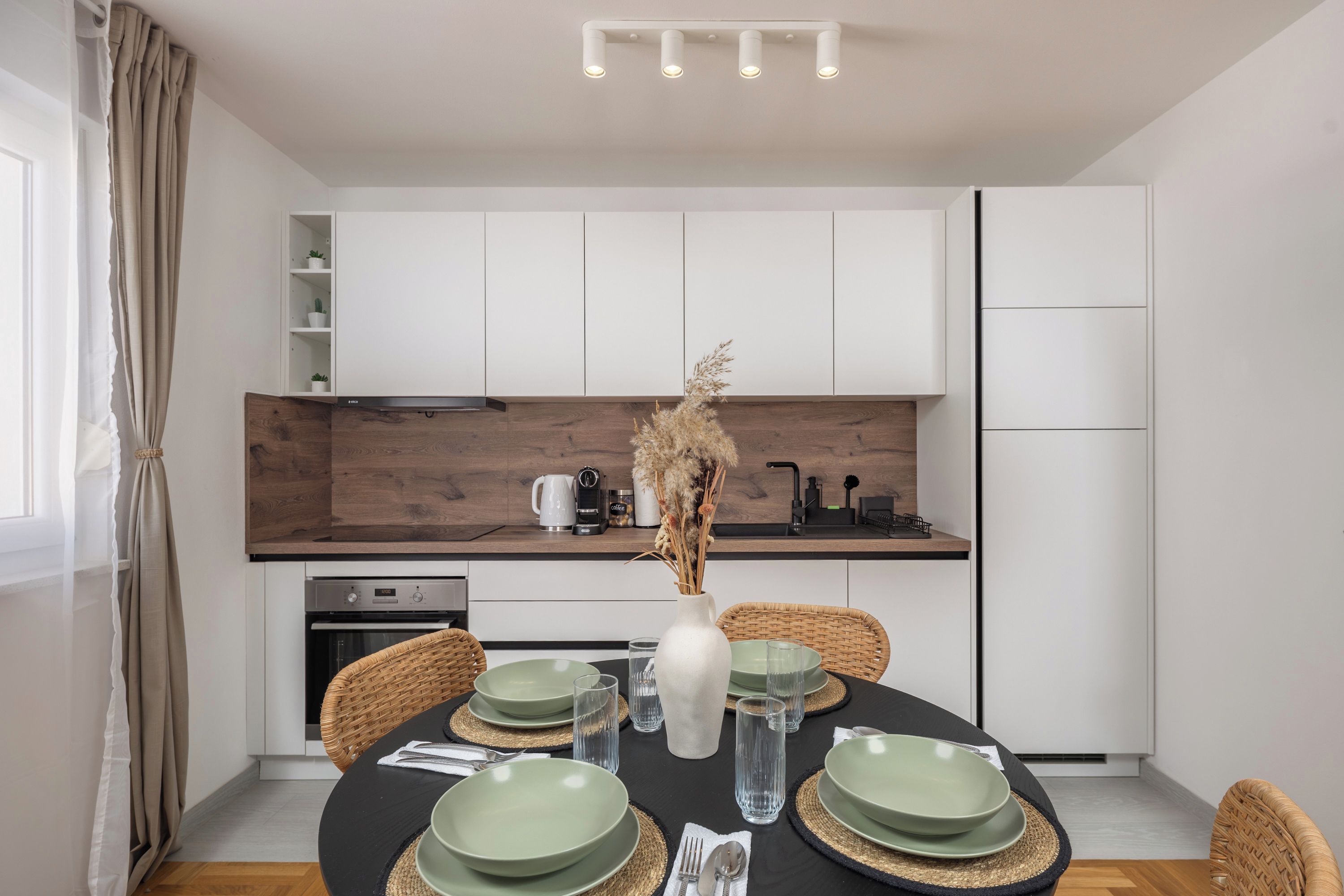A modern kitchen with white cabinets, a wooden countertop, and a dining area with a round table set for four.