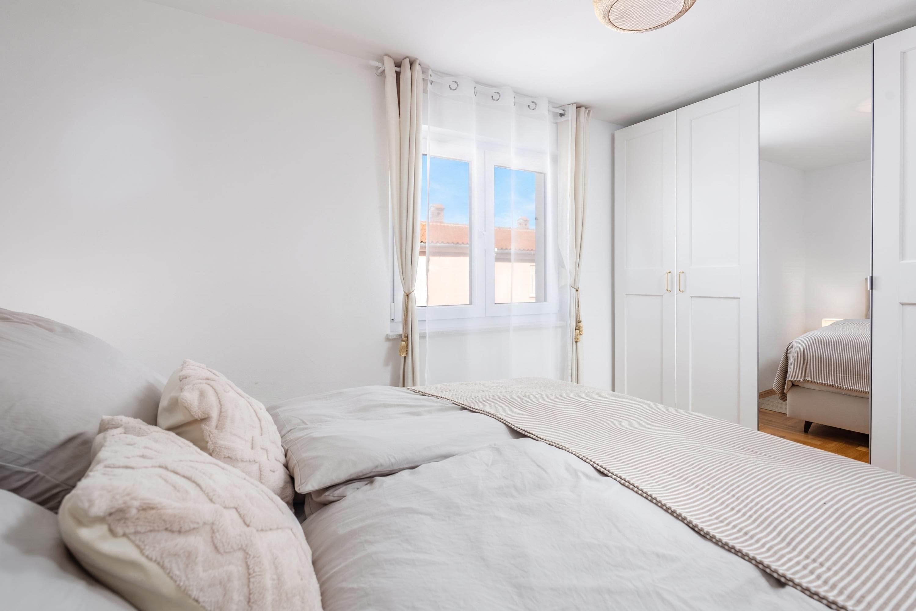 A bedroom with a bed, a wardrobe, and a window with curtains.