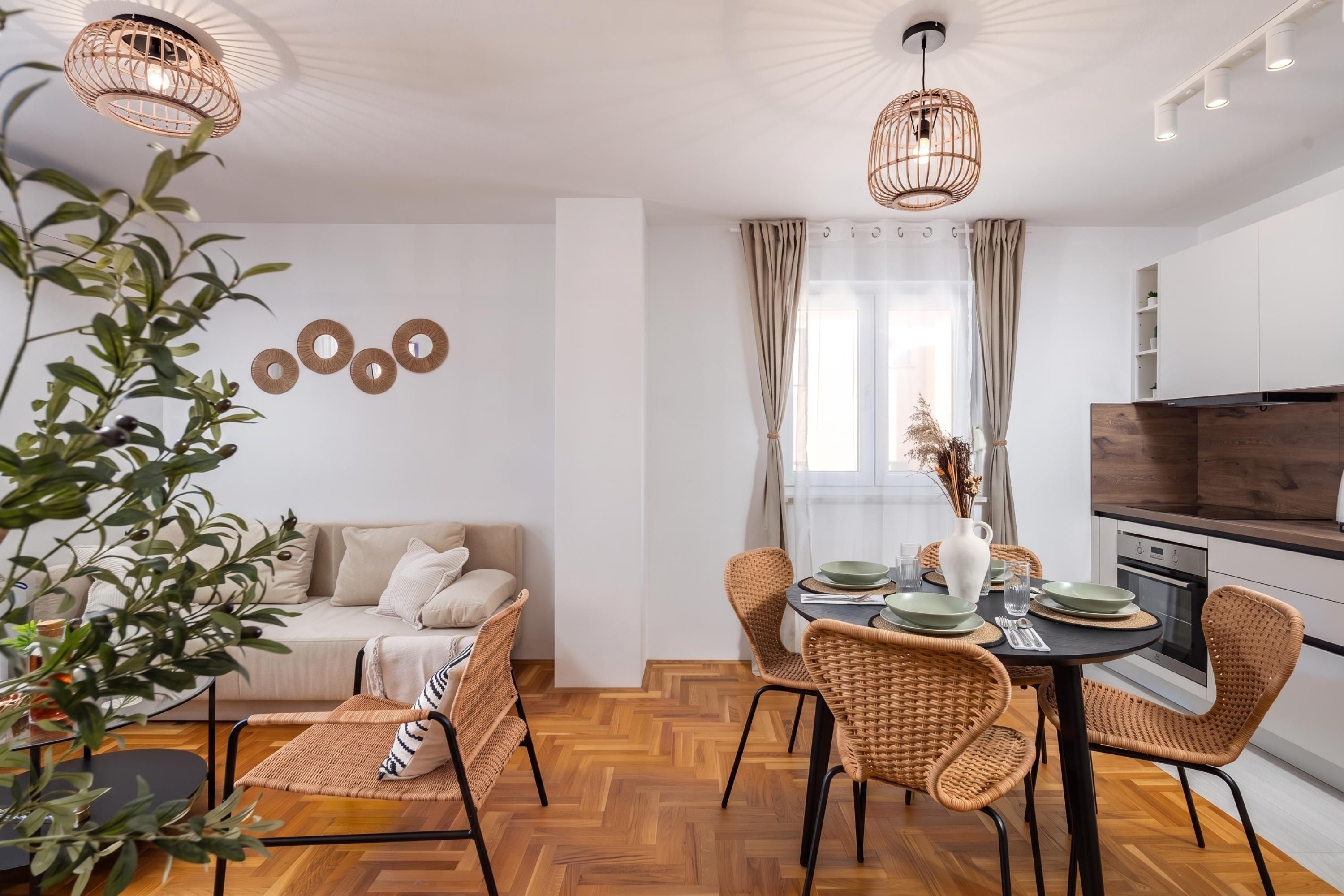 A modern kitchen with a dining area, featuring a herringbone floor pattern, wicker chairs, and pendant lighting.