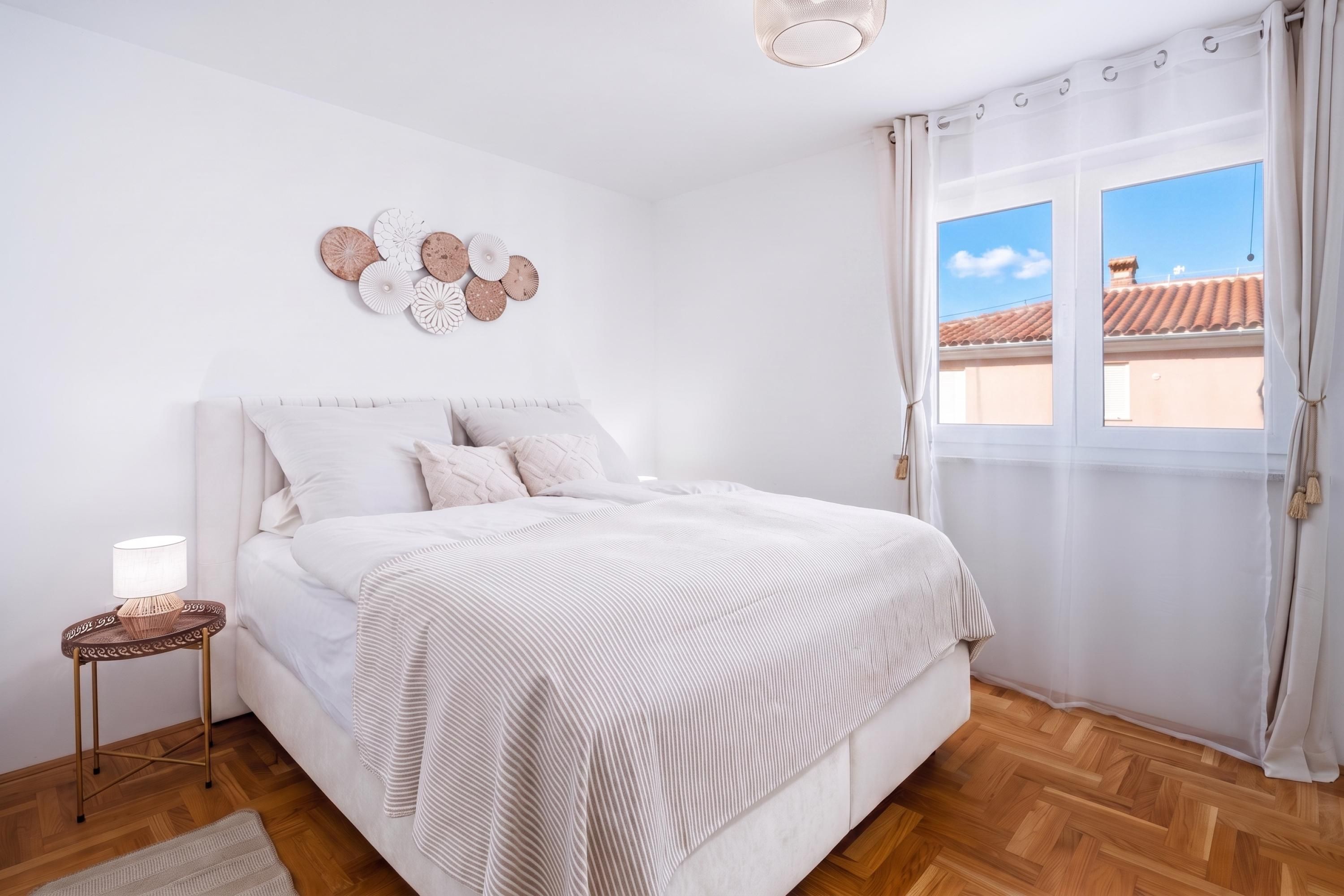 A bedroom with a bed, a bedside table with a lamp, a decorative wall piece, and a window with curtains.