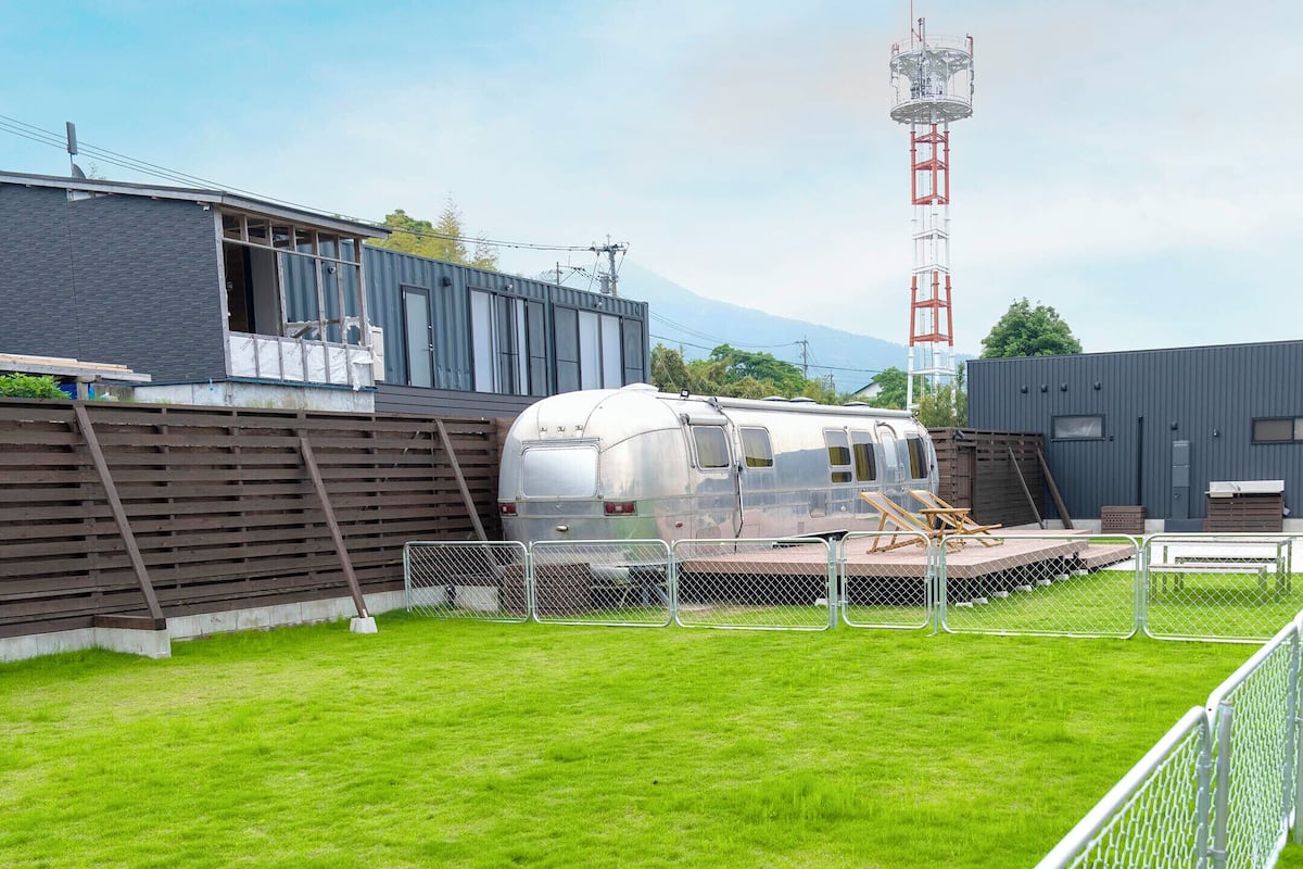 A modern building with a balcony, a trailer, and a fenced area with a grassy lawn.