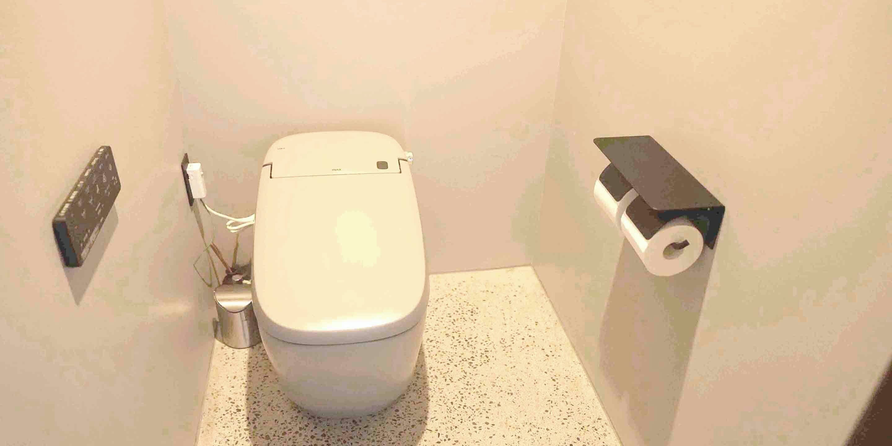 A small bathroom with a toilet, a hand dryer, and a toilet paper holder.