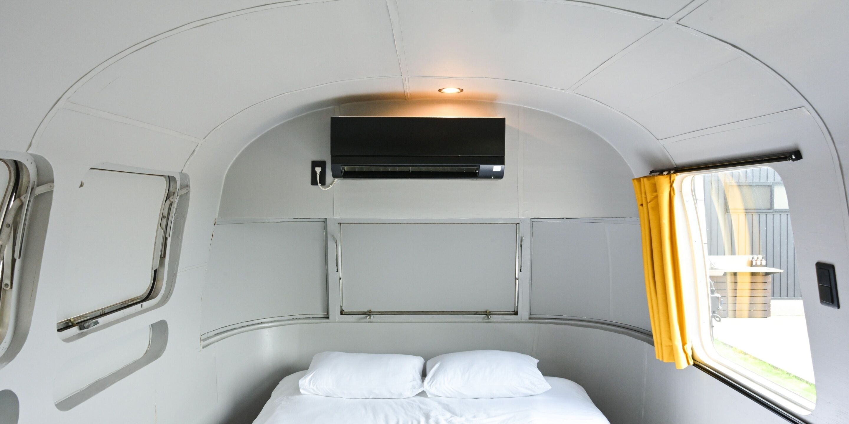 Ein kompakter, bogenförmiger Innenraum mit einem Bett, einer Wandklimaanlage und einem Vorhangfenster.