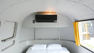 Ein kompakter, bogenförmiger Innenraum mit einem Bett, einer Wandklimaanlage und einem Vorhangfenster.
