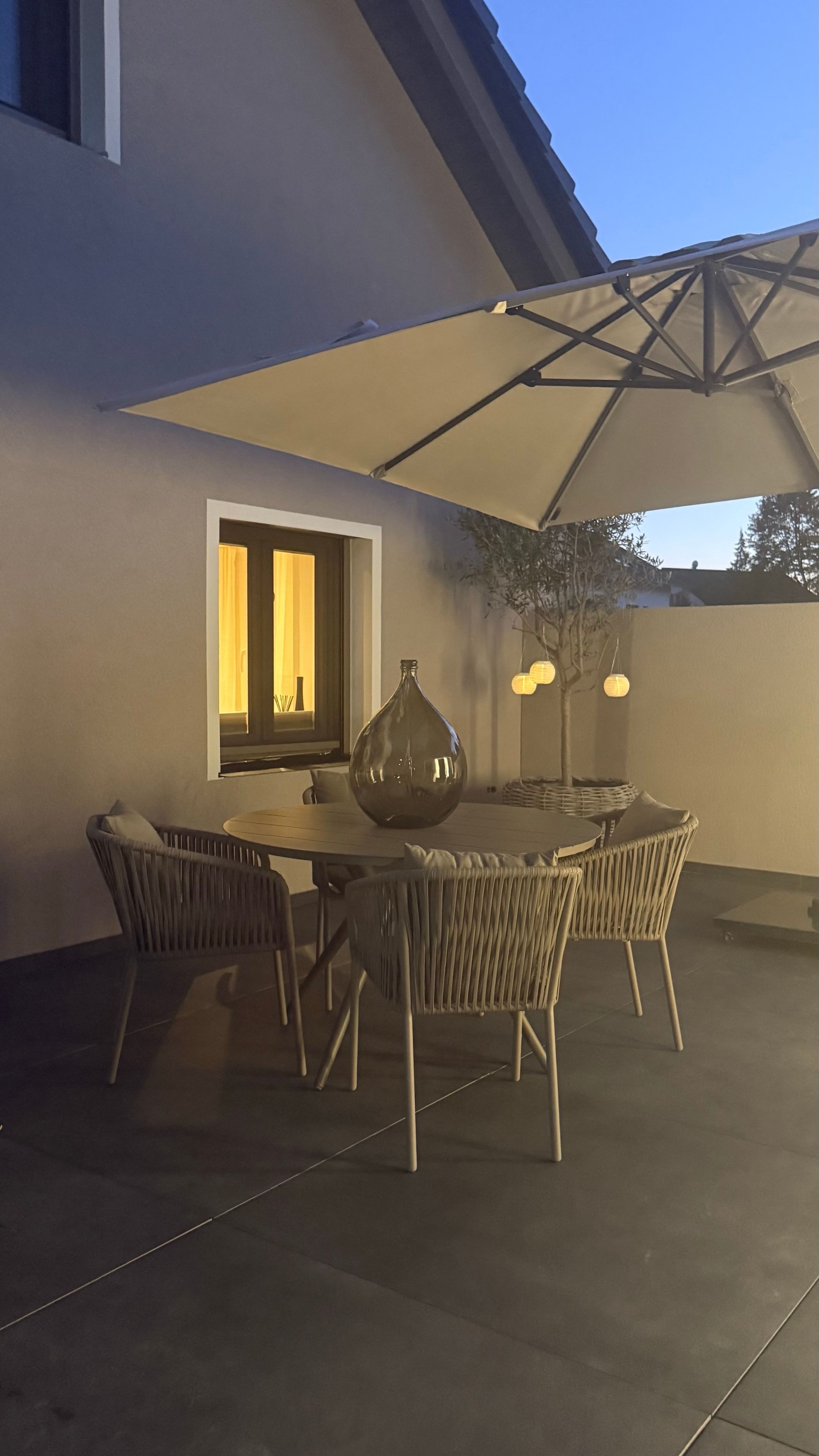 Eine Terrasse im Freien mit Tisch, Stühlen, einer dekorativen Vase und einem großen Sonnenschirm, der Schatten spendet.