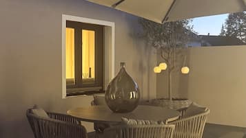 Eine Terrasse im Freien mit Tisch, Stühlen, einer dekorativen Vase und einem großen Sonnenschirm, der Schatten spendet.