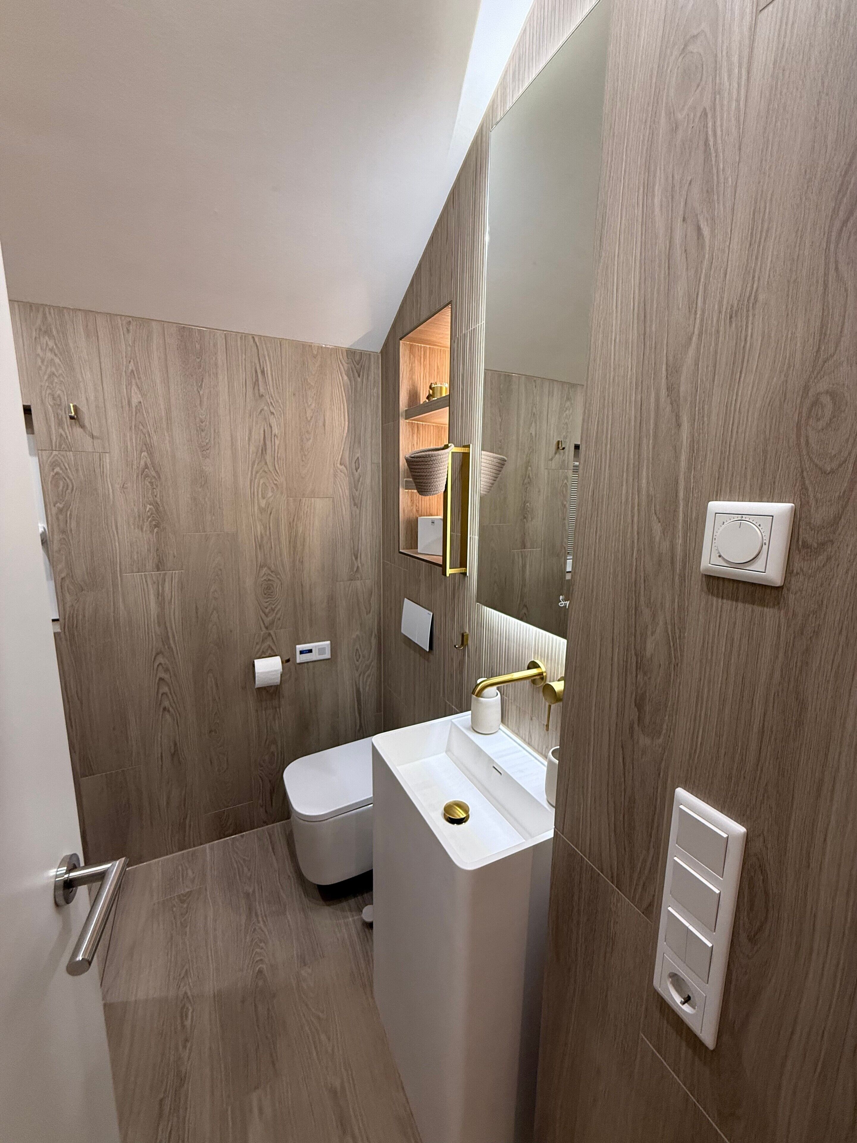 Un baño moderno con pared de madera, lavamanos blanco y un inodoro.