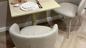 A dining area with a table set for two, a chair, and a window with blinds.
