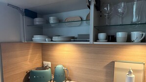 A kitchen with a wooden countertop, a toaster, a kettle, a paper towel dispenser, and glassware on shelves.