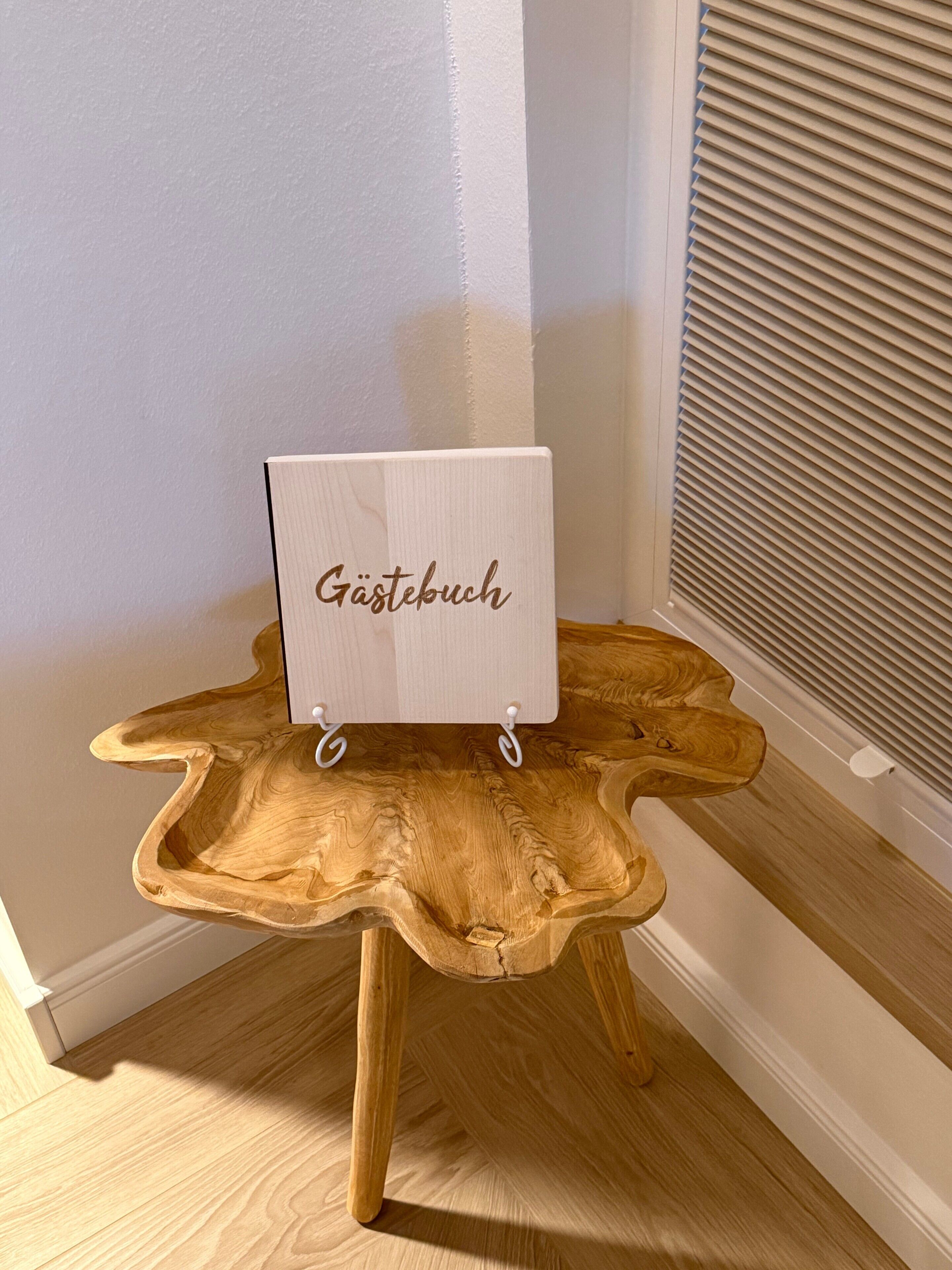 Ett litet bord av trä, med en skylt där det står ”Gästebuch” och ett fönster med persienner.