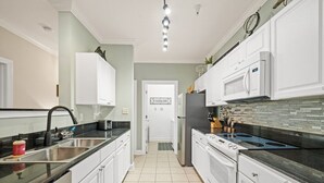 Ett modernt kök med vita skåp, en diskho i rostfritt stål, en mikrovågsugn och en spis.