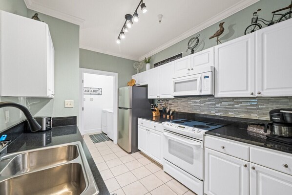 A modern kitchen with white cabinets, a stainless steel sink, a microwave, a stove, and a refrigerator. - Park Ave 112 - First Floor Condo (Foley)