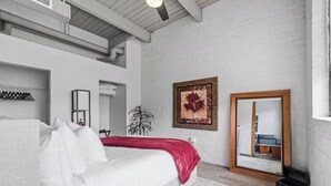 Ein Schlafzimmer mit einem weißen Bett, einer roten Decke, einem großen Spiegel und einem gerahmten Bild an der Wand.