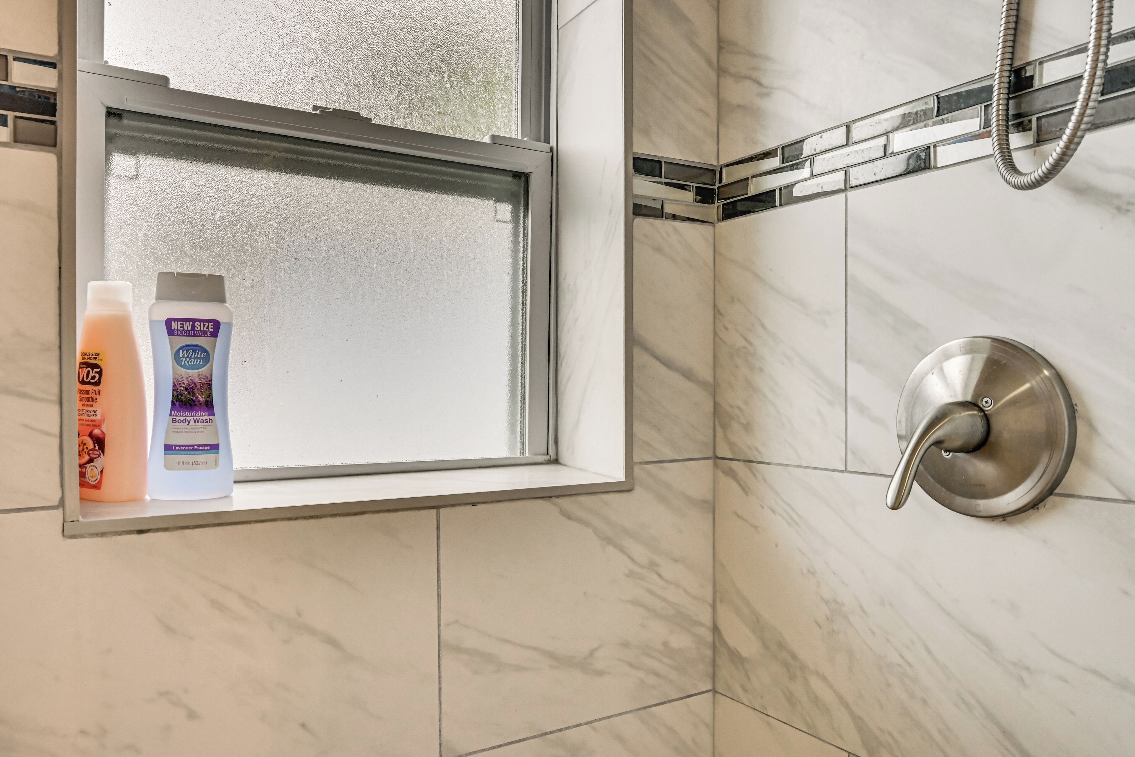 A bathroom with a window, a shower, and toiletries on the windowsill.