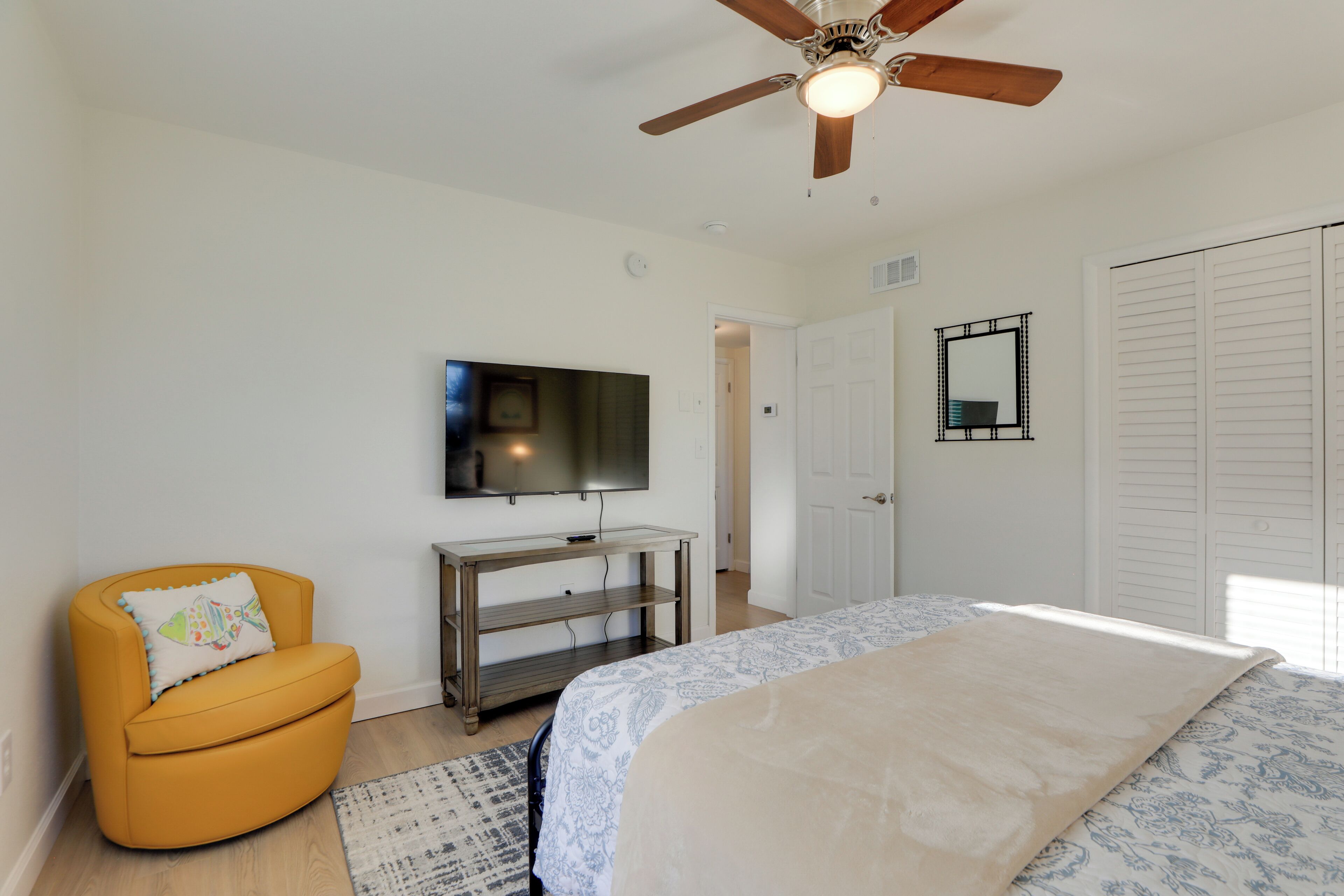 A bedroom with a bed, a TV, a ceiling fan, a chair, and a wardrobe.