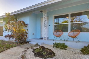 Une maison avec un porche, deux chaises, un rocher et des plantes.