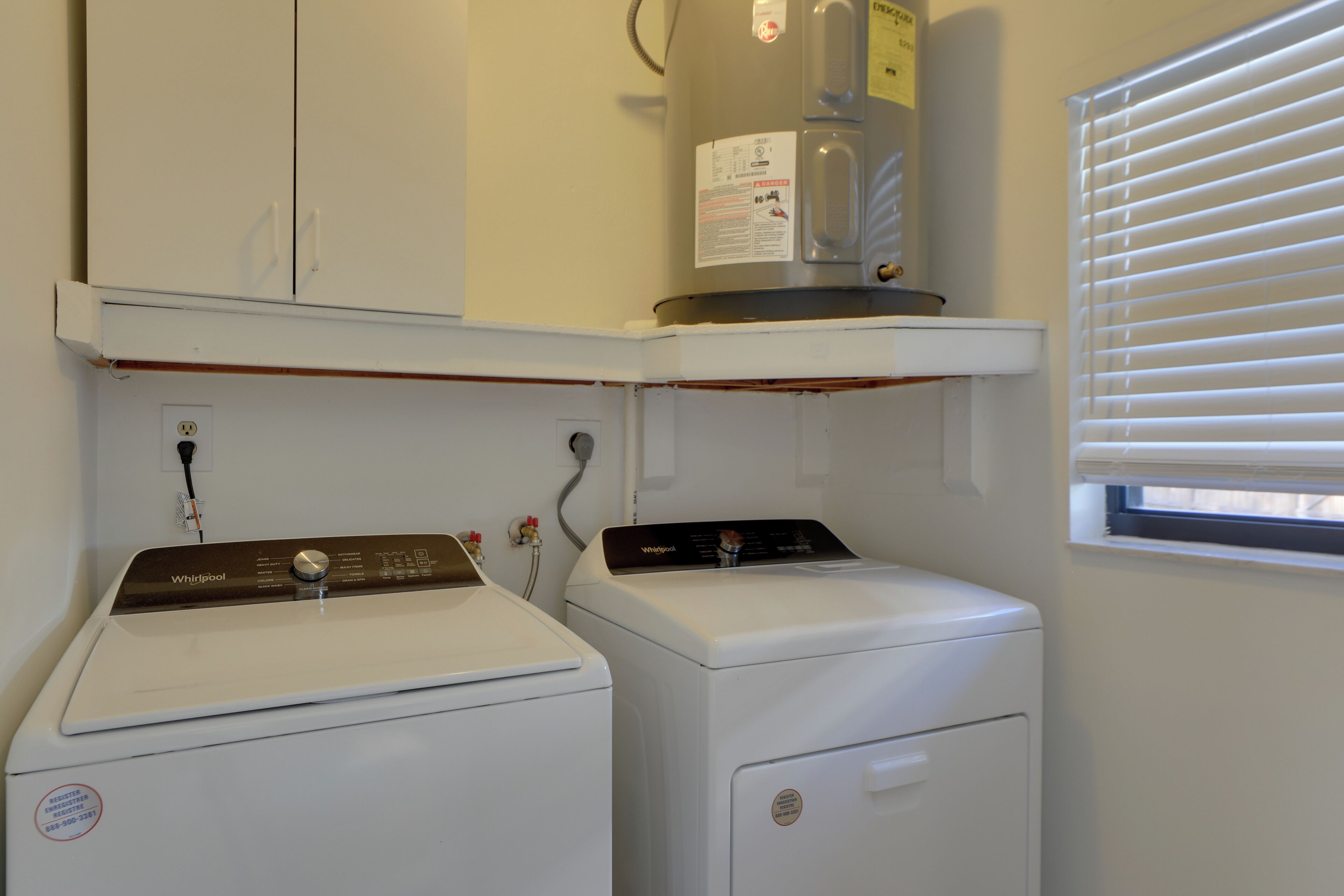 A laundry area with two front-loading washers, a water heater, and a window with blinds.