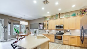 A modern kitchen with wooden cabinets, a central island, stainless steel appliances, and a dining area with chairs and a table. - Patio & Home Gym! Augusta Ranch Golf Home (Mesa)