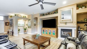 A living room with a fireplace, leather sofas, a wooden coffee table, and a ceiling fan. - Patio & Home Gym! Augusta Ranch Golf Home (Mesa)