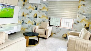 A modern living room with a flat-screen TV, beige sofas, a round coffee table, and marble-patterned walls.