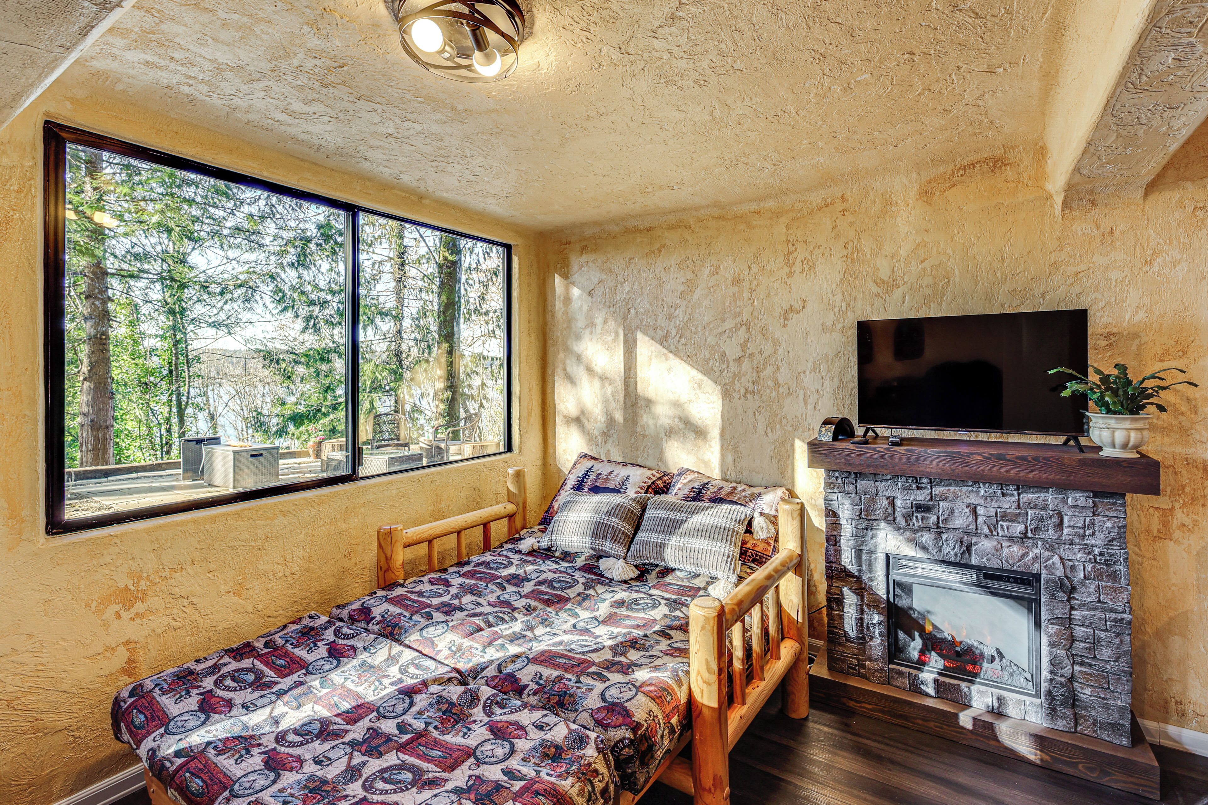 A room with a bed, a fireplace, a TV, and a large window.