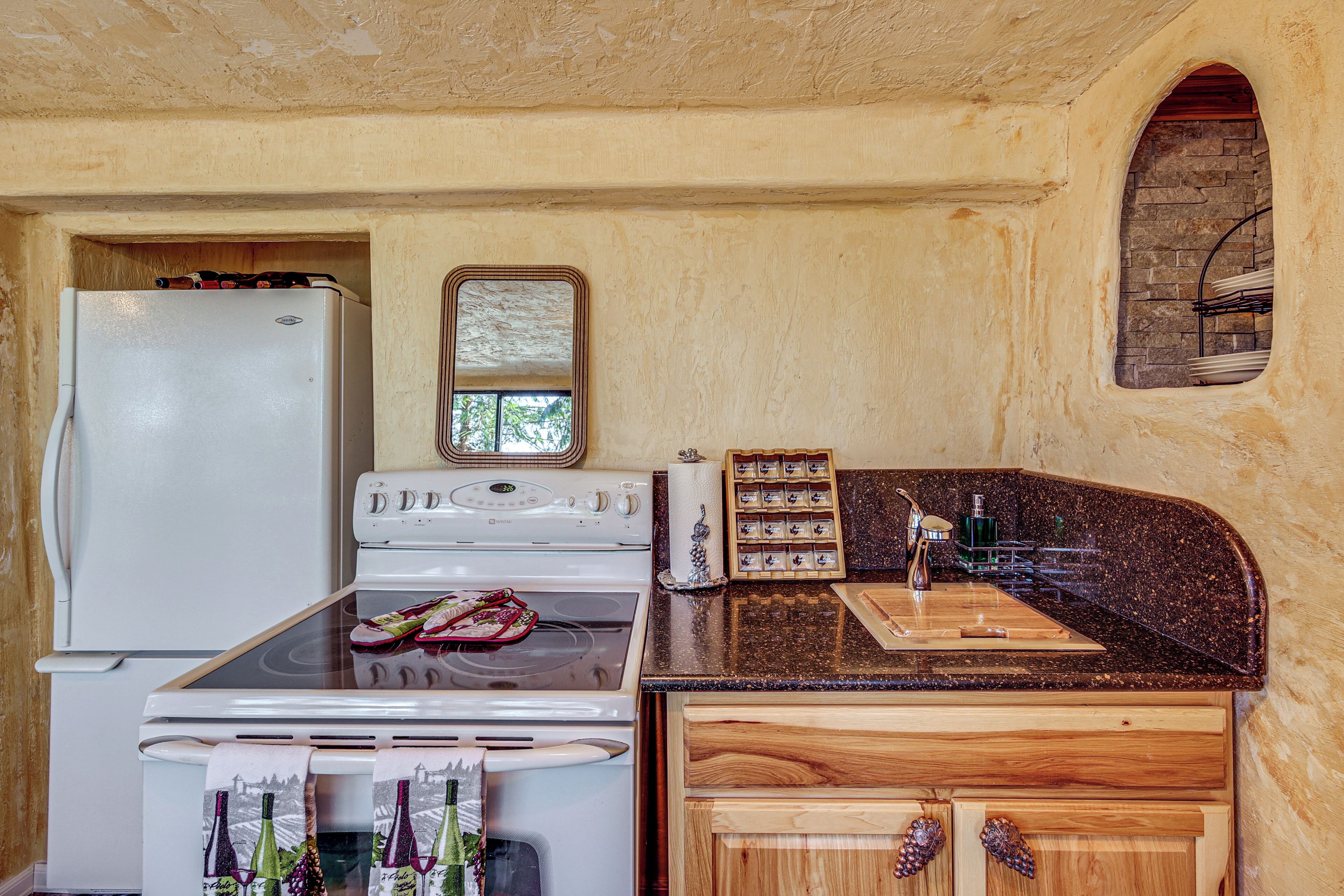 A kitchen with a white refrigerator, stove, and oven, wooden cabinets, a granite countertop, and a small window.