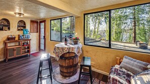 A rustic interior with a wooden barrel table, a sofa, and a view of the forest through large windows. - Walk to Beach! Scenic 'wine Studio' in Gig Harbor (Gig Harbor)
