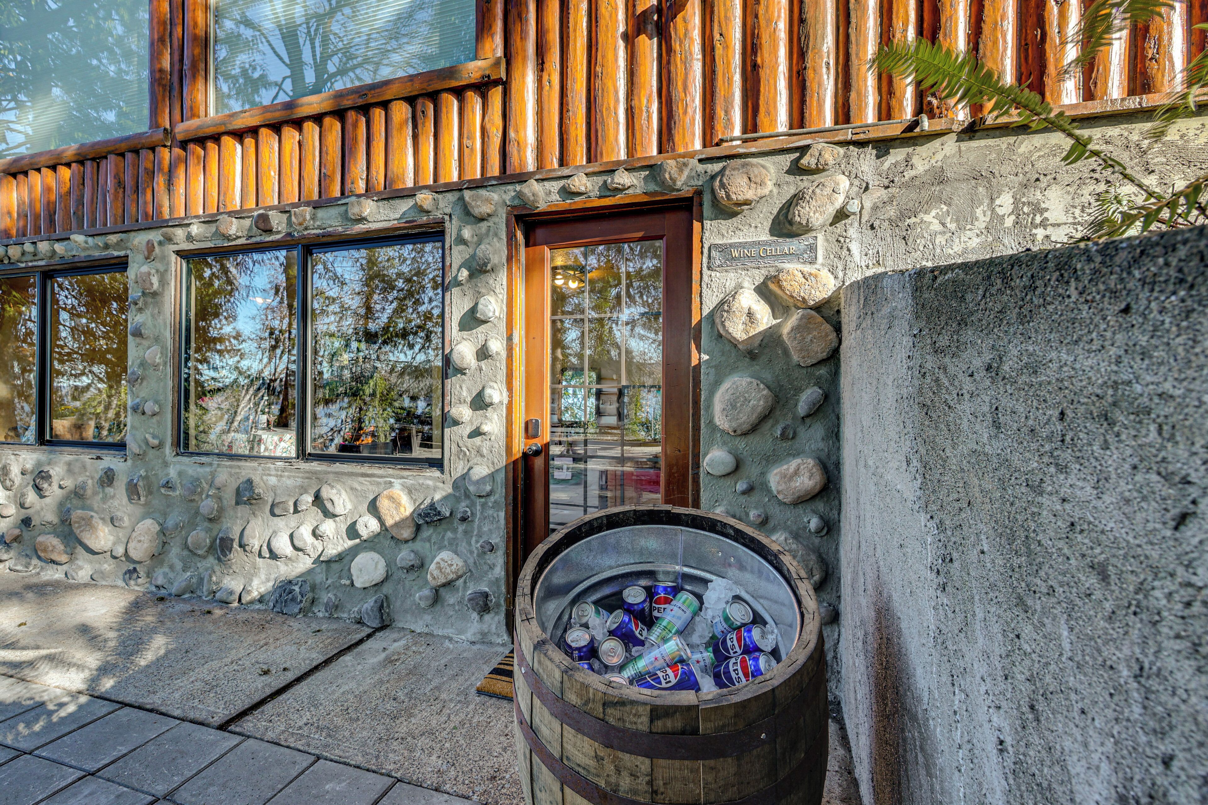 Een stenen gebouw met een houten deur en ramen, een vat met blikken en een bord waarop staat 'Wine Cellar'.