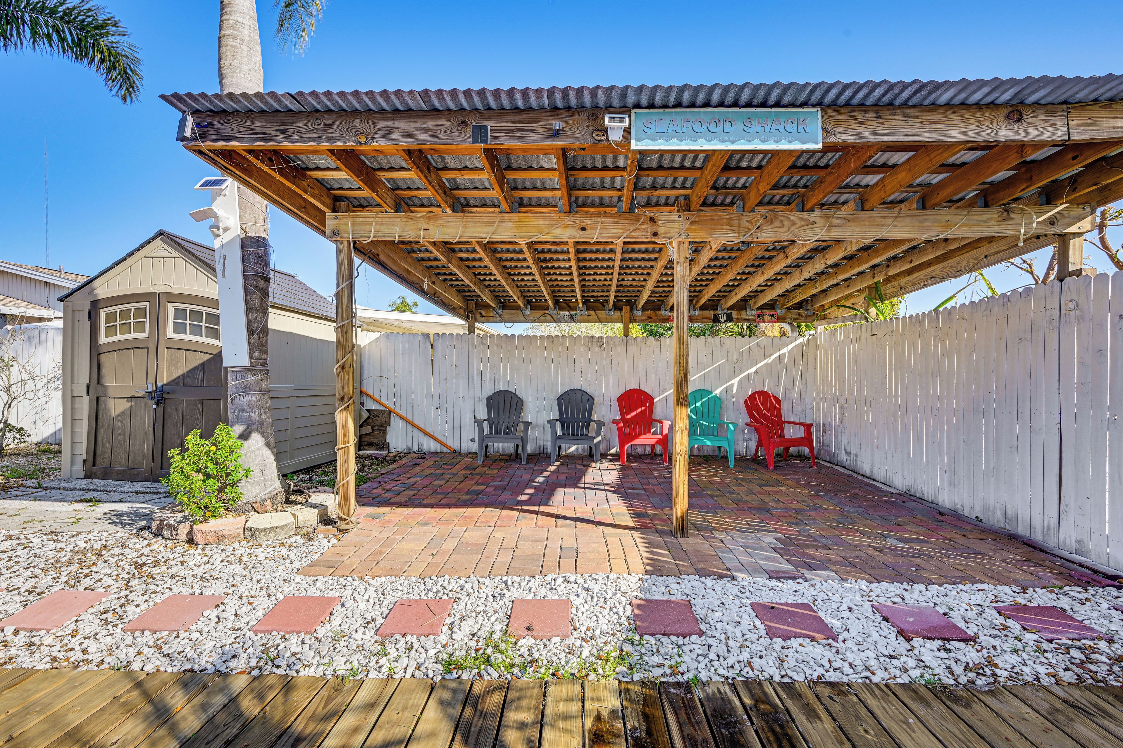 A covered patio area with a wooden pergola, a sign reading 'SEAFOOD SHACK,' and several Adirondack chairs.